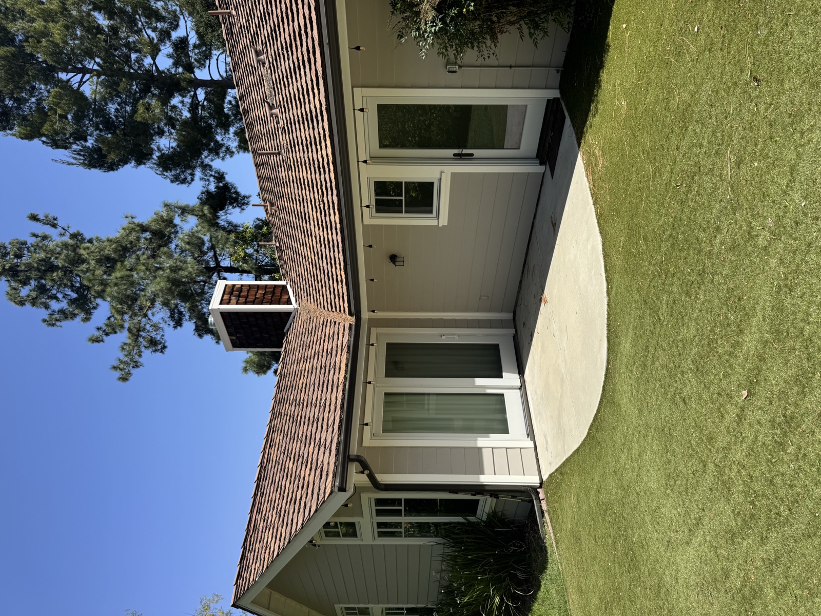 Cedar-shake-clad chimney with copper cap and flashing meeting a clay tile roof — bespoke structural envelope by PBG, Los Angeles.