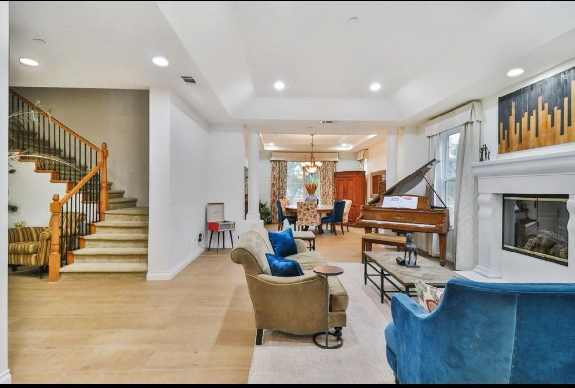 Living room with cast-stone fireplace, custom mantel millwork, and grand piano — finished interior by PBG, Los Angeles residential.