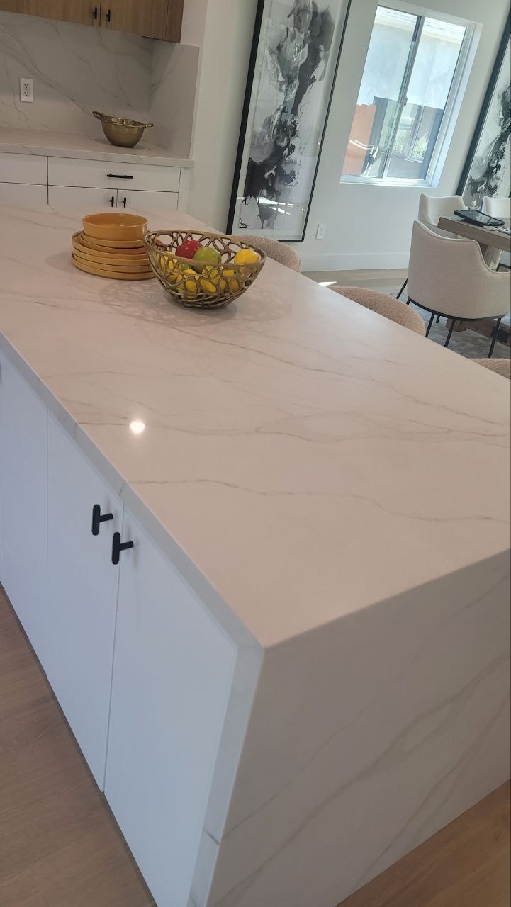 Angled view of waterfall-edge Calacatta quartz island with mitered seam, staged with fruit bowl — PBG custom kitchen, Los Angeles.