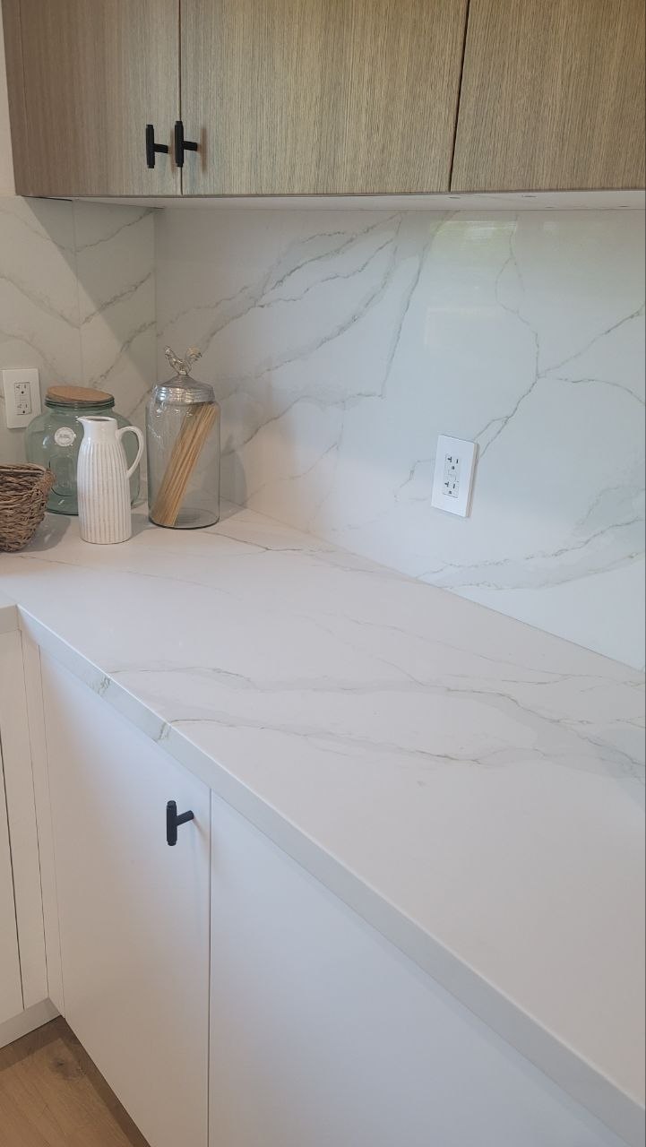 Kitchen counter run — Calacatta quartz counter with full-height slab backsplash and light-oak upper cabinets over white base — PBG custom kitchen.