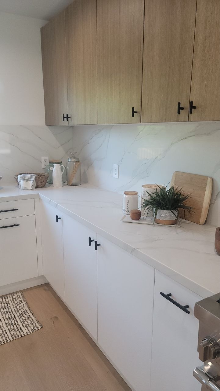 Wide L-run view of modern kitchen — light-oak upper cabinets, matte-white lowers, Calacatta quartz counters and backsplash, matte-black hardware — PBG custom build, Los Angeles.