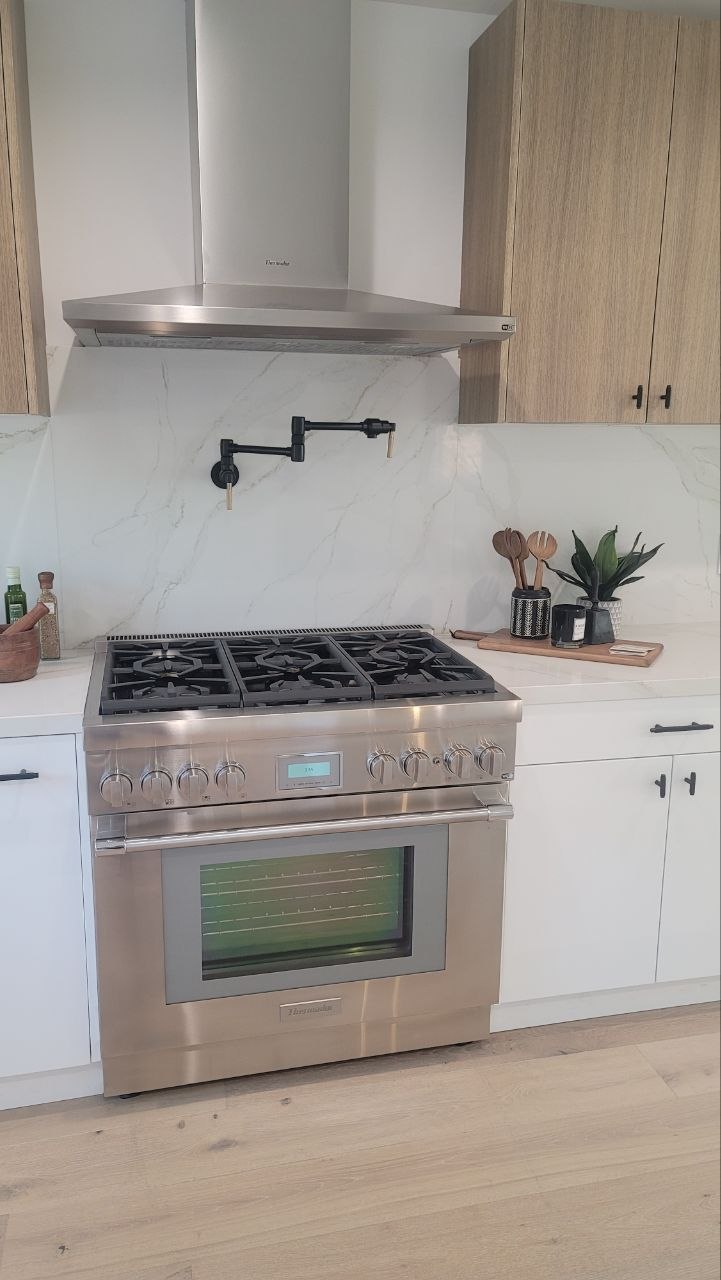 Range wall hero — Thermador pro gas range and stainless hood with pot filler and full-height Calacatta quartz slab backsplash — PBG custom kitchen, Los Angeles.