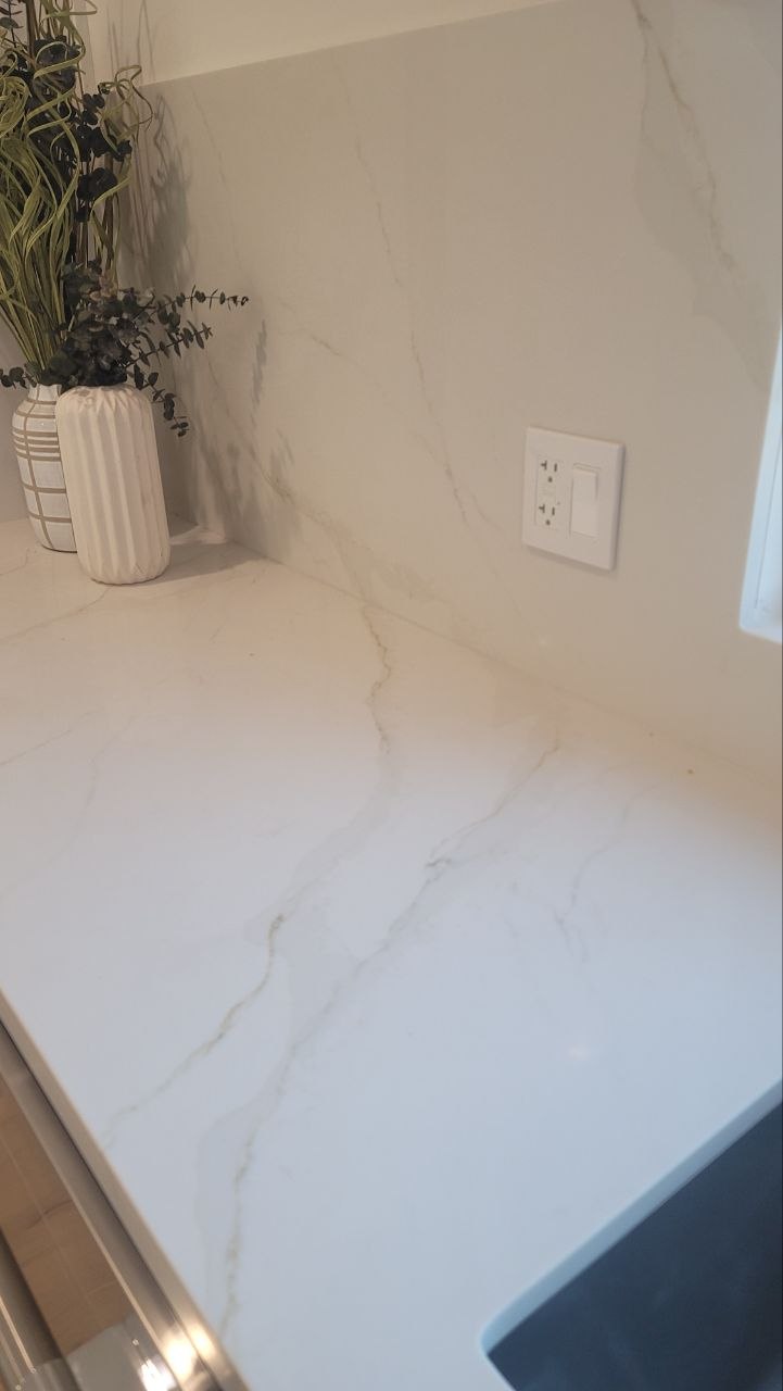 Detail — Calacatta-vein slab counter flowing into full-height slab backsplash with decorative outlet — PBG custom kitchen, Los Angeles.