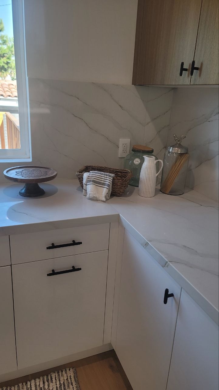 Modern kitchen pantry corner in natural window light — Calacatta slab counter and backsplash, light-oak upper, matte-white lowers, matte-black hardware — PBG custom kitchen, Los Angeles.