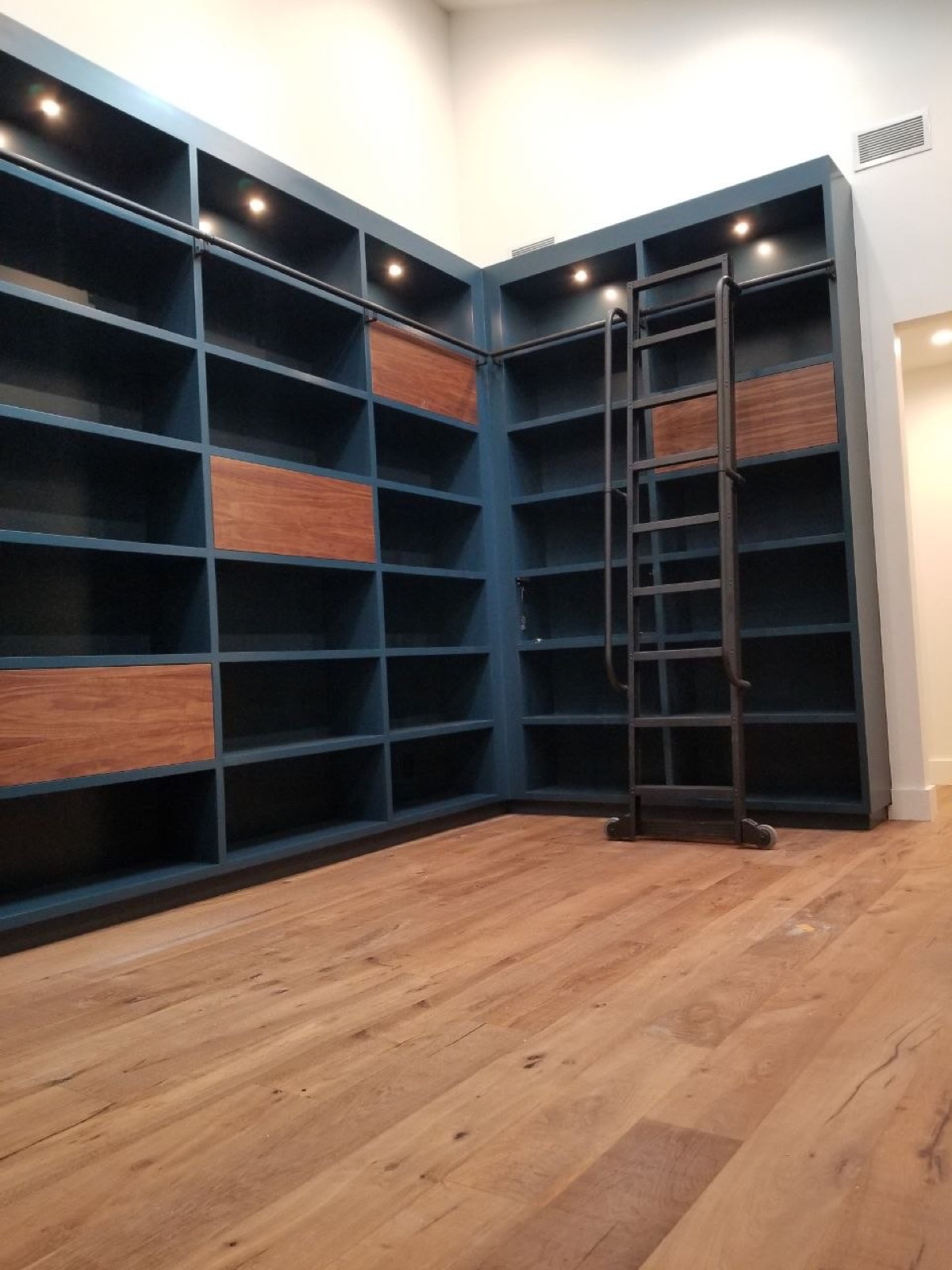 Two-story custom navy library with walnut inlays, rolling iron ladder, and wide-plank oak floors — bespoke luxury residential build by PBG, Los Angeles.