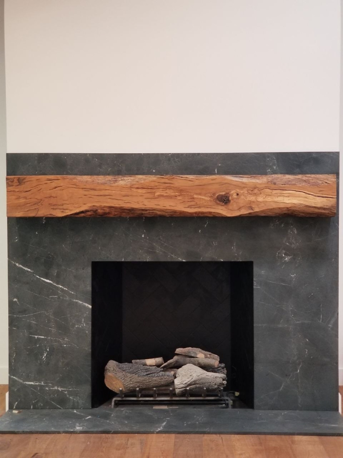 Custom fireplace with honed soapstone surround and reclaimed live-edge wood mantel — bespoke millwork by PBG, Los Angeles.