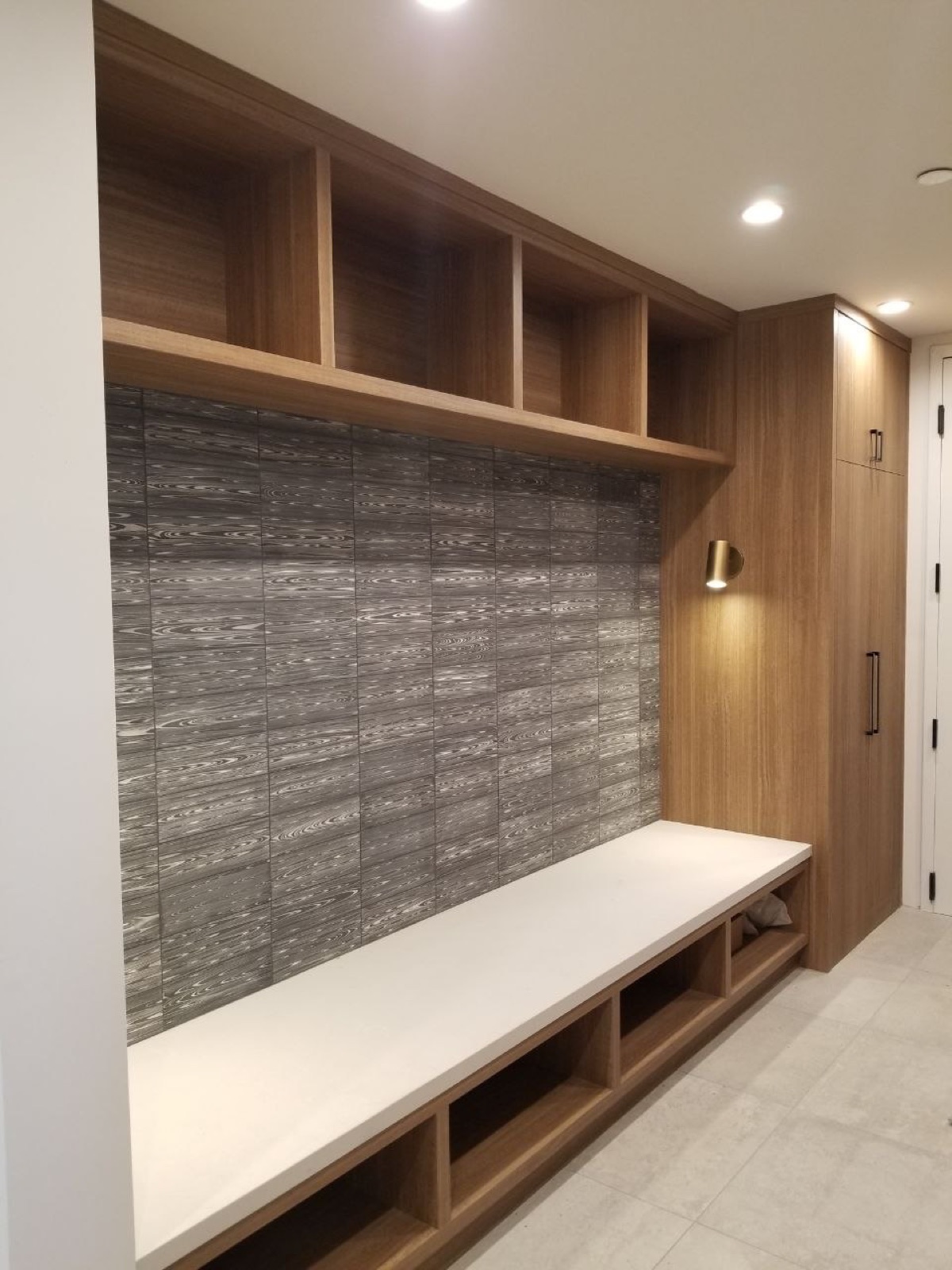 Custom walnut mudroom with textured stone feature wall, floating bench, and brass sconce — bespoke millwork by PBG, Los Angeles.