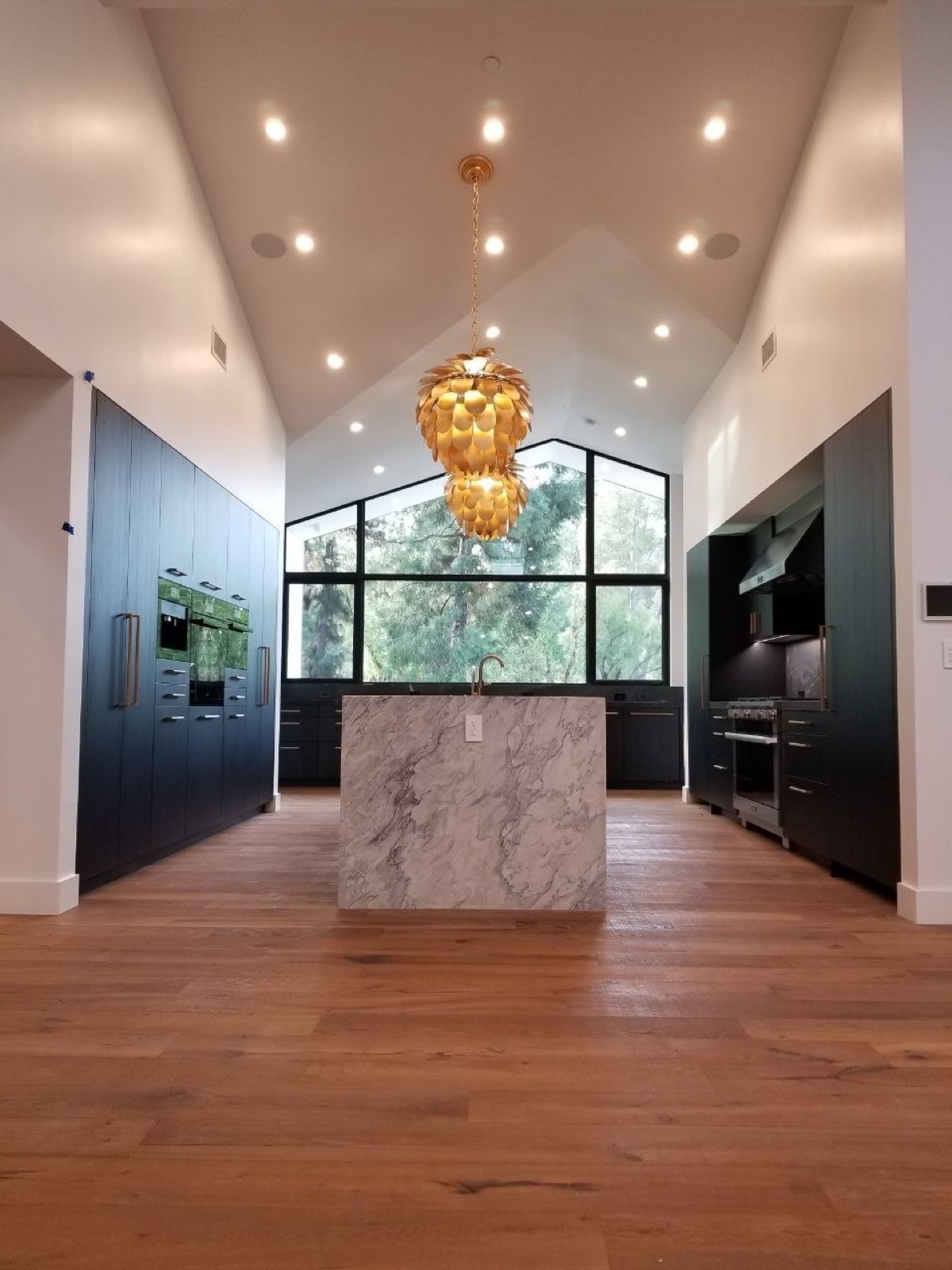 Vaulted modern kitchen with waterfall marble island, gold pendant lighting, and gabled window wall — custom luxury residential build by PBG, Los Angeles.