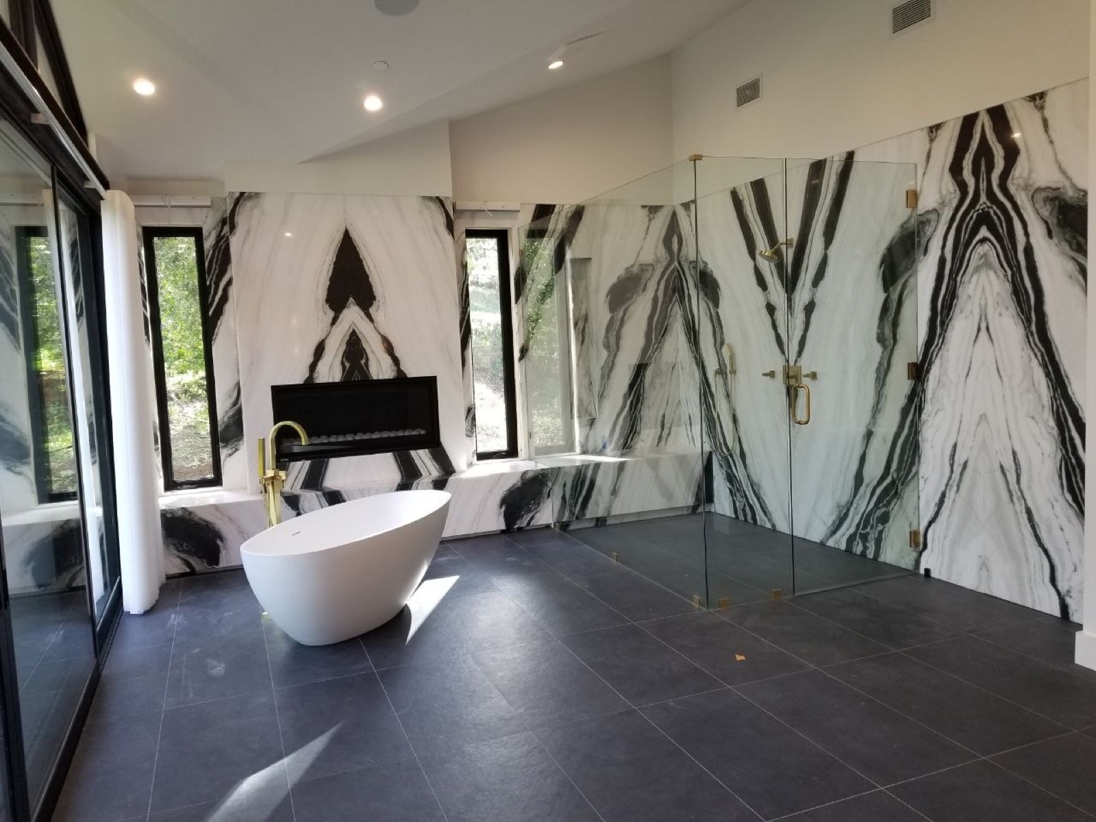 Master bathroom with bookmatched panda-marble feature wall, freestanding stone tub, and glass shower under vaulted ceiling — custom luxury residential build by PBG, Los Angeles.