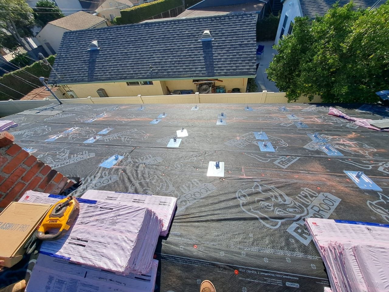 Angled view of RhinoRoof U20 underlayment near the ridge with tile clips pre-set and original shingles being replaced — process detail from a PBG residential re-roof.