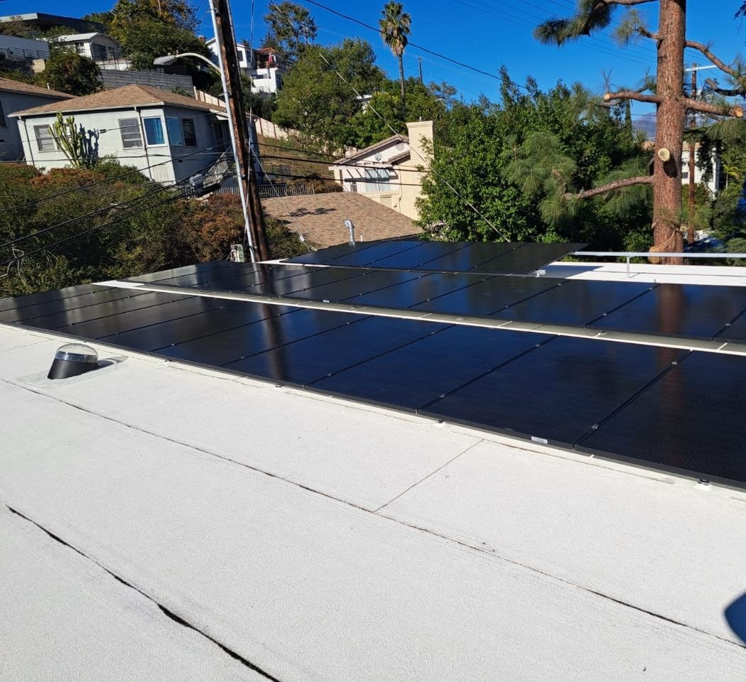 Flat-roof residential solar array on white membrane with hillside neighborhood context — solar-integrated build by PBG, Los Angeles.