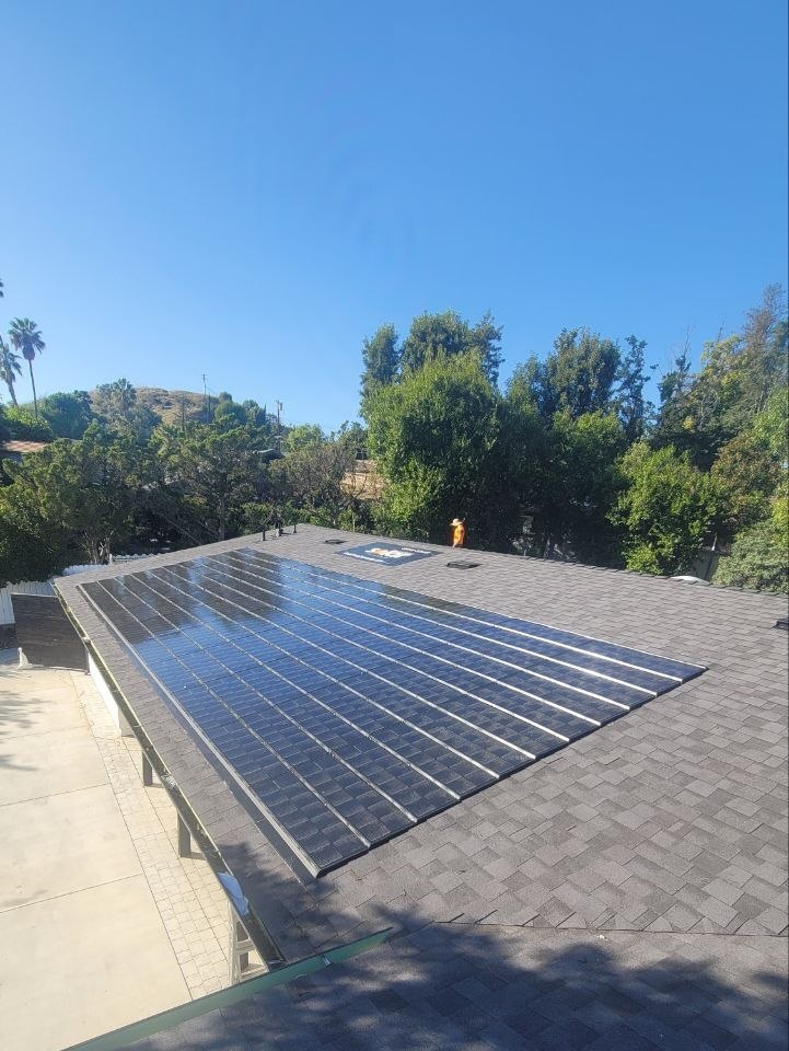 Flush-mount residential solar array on a sloped shingle roof with hillside and palm-tree Los Angeles context — solar-integrated build by PBG.