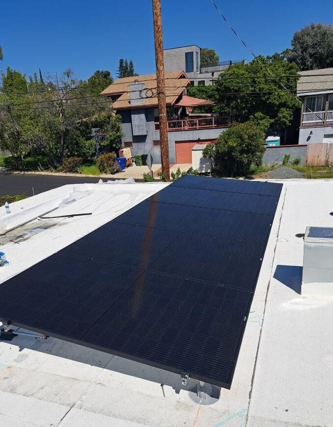 All-black solar array on a bright white flat-roof membrane with residential Los Angeles neighborhood context — solar-integrated build by PBG.