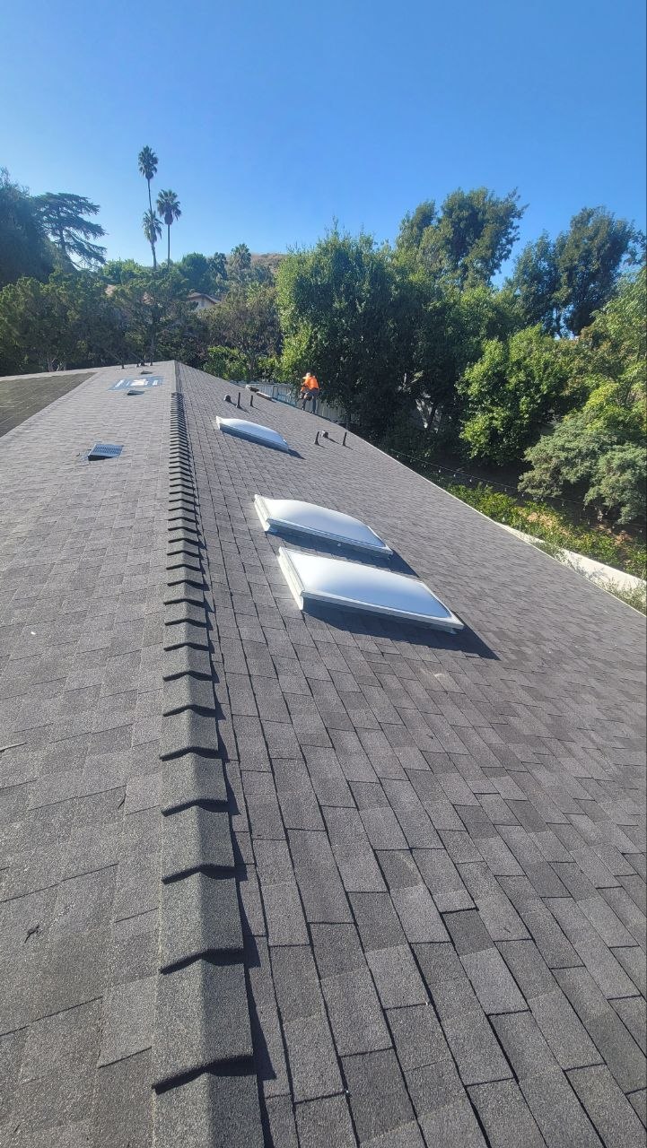 Gray architectural asphalt shingle roof with new ridge cap and three domed skylights — PBG roofing work.