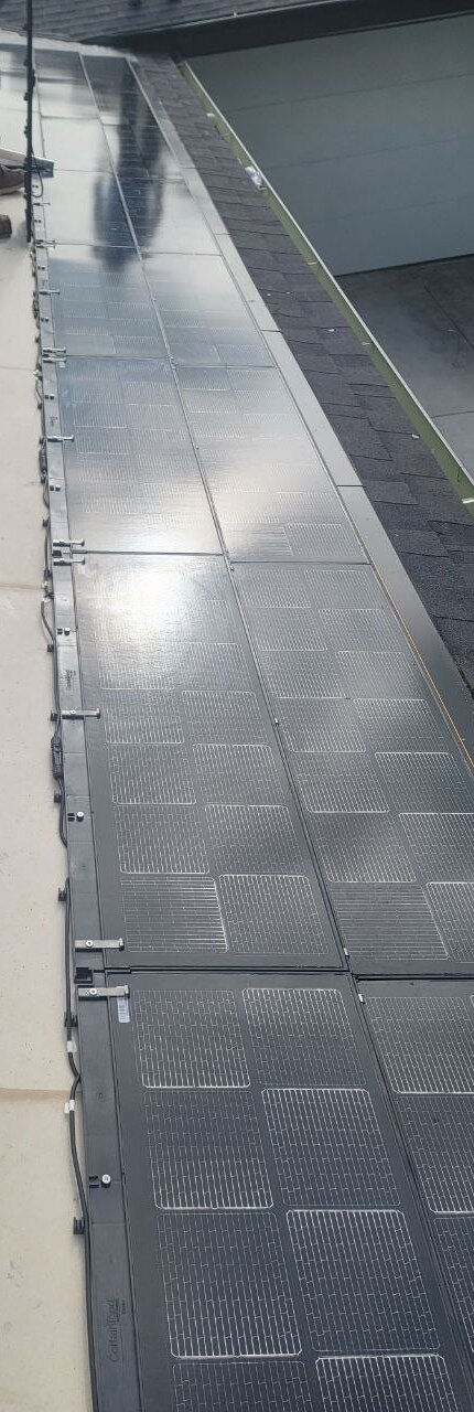 Starter-row detail of BIPV solar-integrated panels transitioning to composition shingle, with clip system visible — technical craft on a PBG custom residential build, Los Angeles.