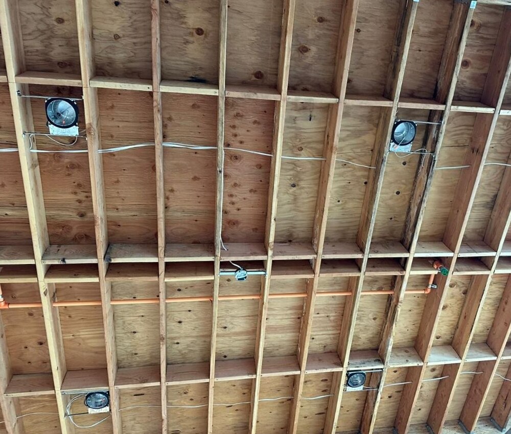 Structural ceiling detail — engineered rafter grid with plywood decking, Simpson strap ties, copper plumbing, and can-light rough-ins routed through the framing on a PBG custom residential build, Los Angeles.